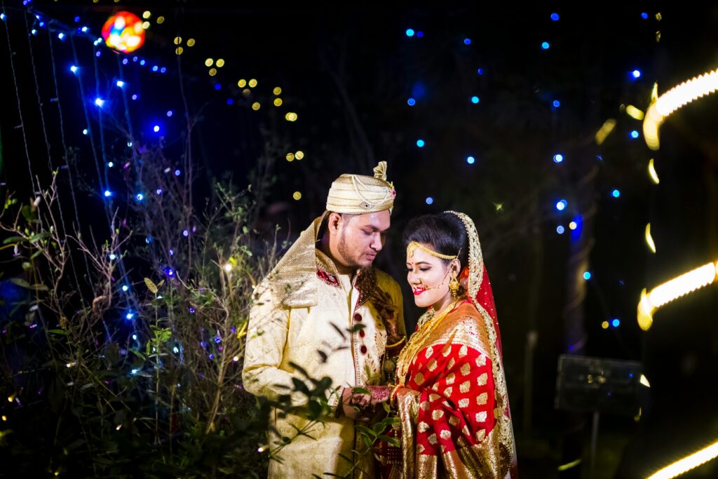 Beautiful couple enjoying their wedding night in traditional attire, surrounded by colorful lights.