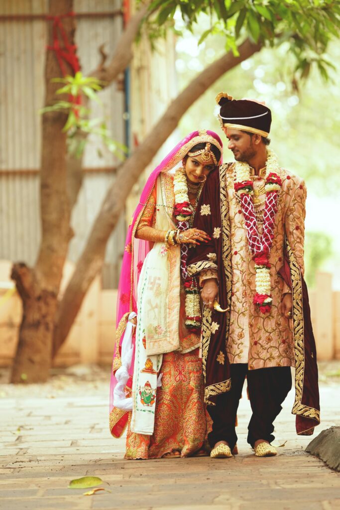 A joyful couple celebrates their traditional Indian wedding in vibrant outdoor attire.