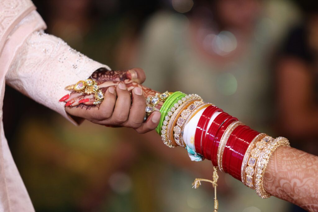 Close-up of couple holding hands with intricate henna and bangles during a traditional Indian wedding ceremony.
