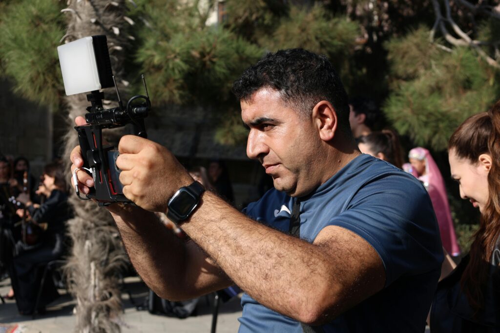 A man holding a handheld camera rig outdoors, capturing a scene in a sunny setting.