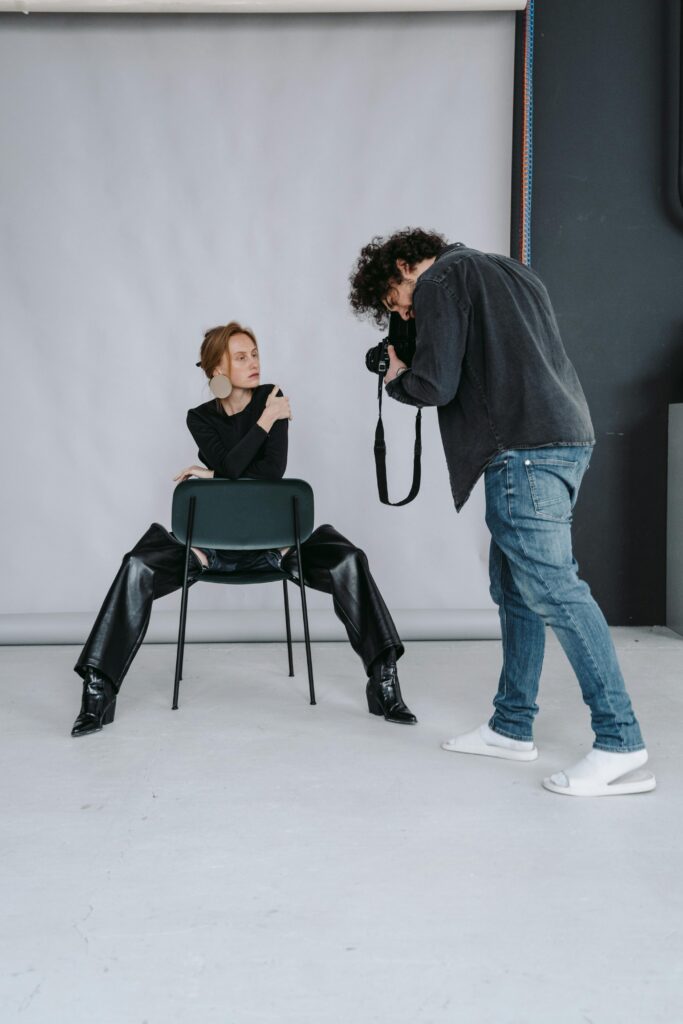 A professional photoshoot in a studio with a model posing on a chair.