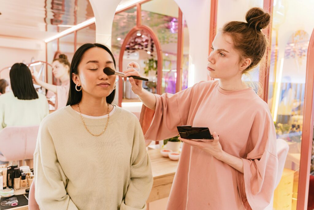 Asian woman receiving makeup from artist in bright, modern beauty salon.